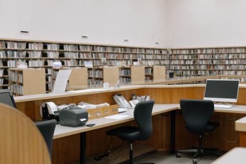 library with walls lined with full bookshelves and large desks with computer and office chairs